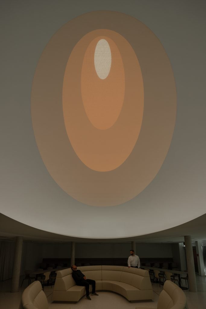 James Turrell installation of a circular ceiling with concentric bands of light, outwards in: off-white, pale orange, and then more saturated orange, and finishing with a small white central white oval.