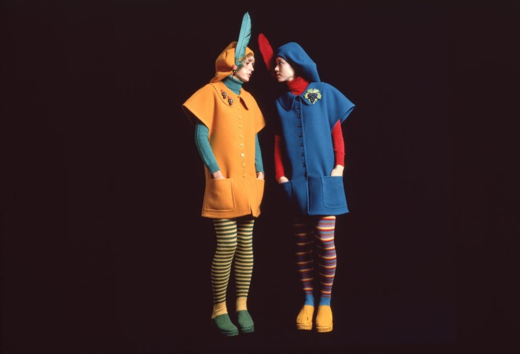 two models wearing colorful 1970s Kenzo fashions stand against a black background 