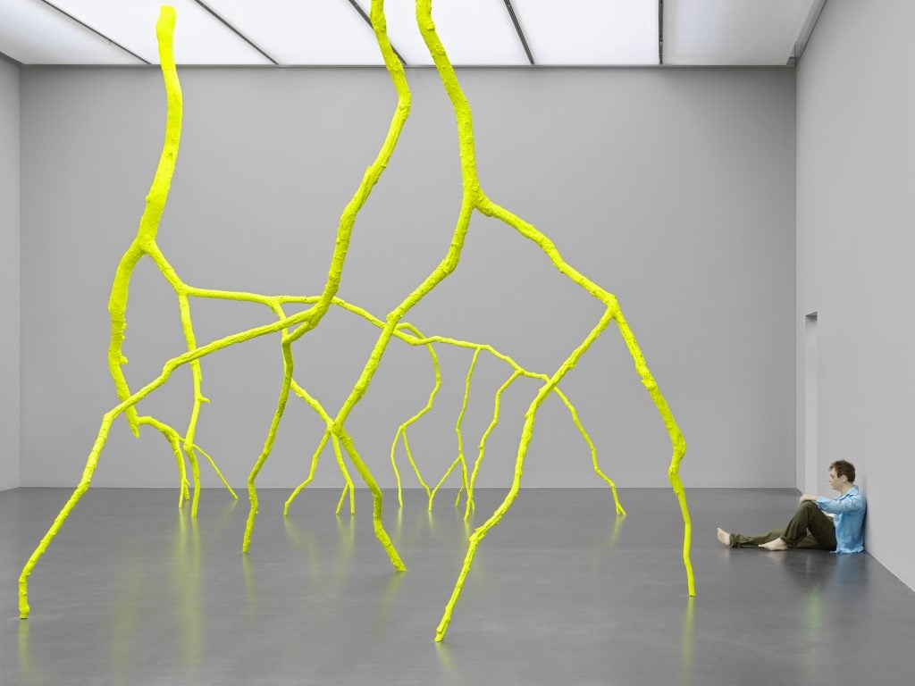 fluorescent branches depicting lightning descend from the ceiling of a gallery over a seated mannequin