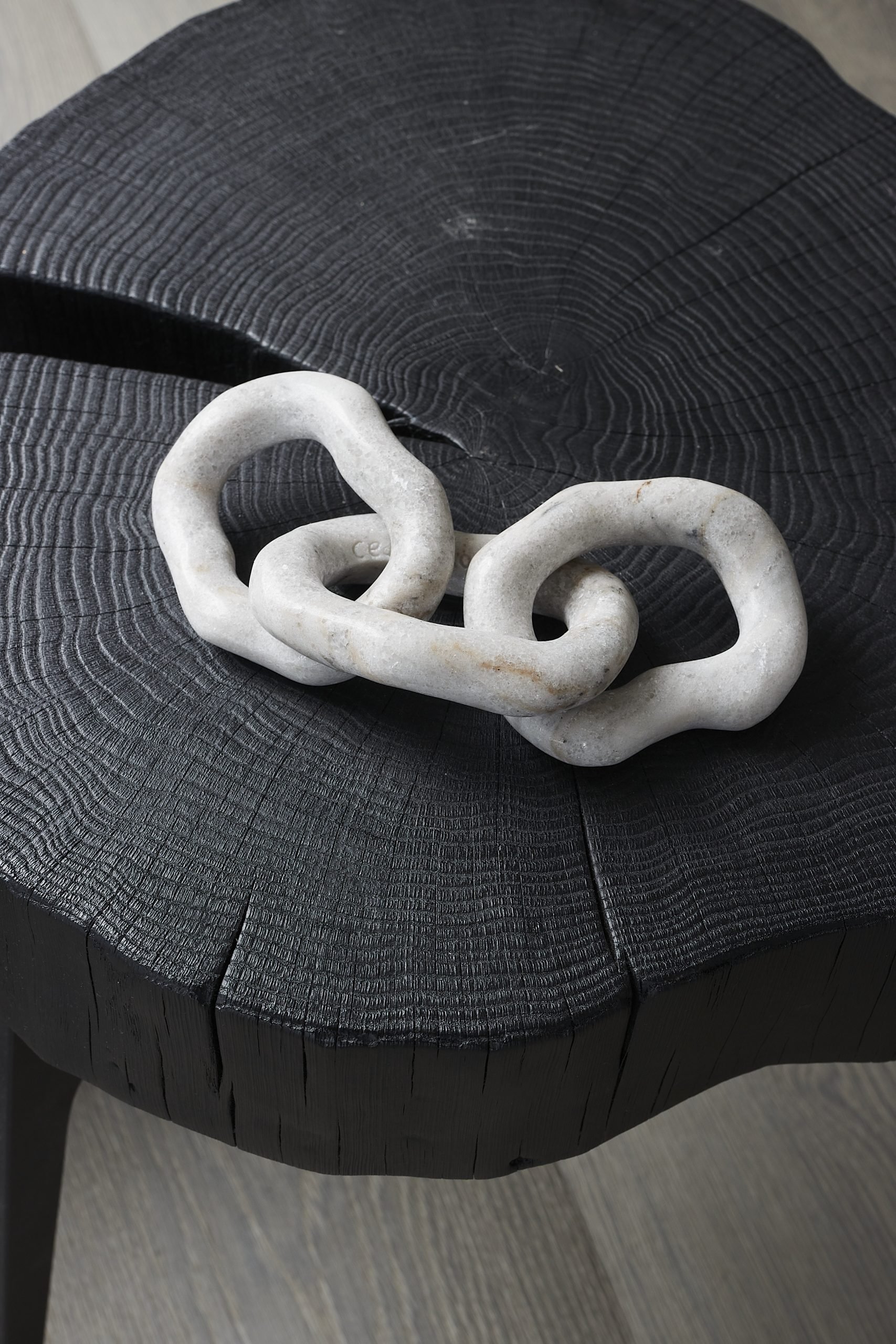 Sculpture featured inside the Krieger x Koukjian collaboration museum in germany, a three link white scul[ture on a black tree cut side table.