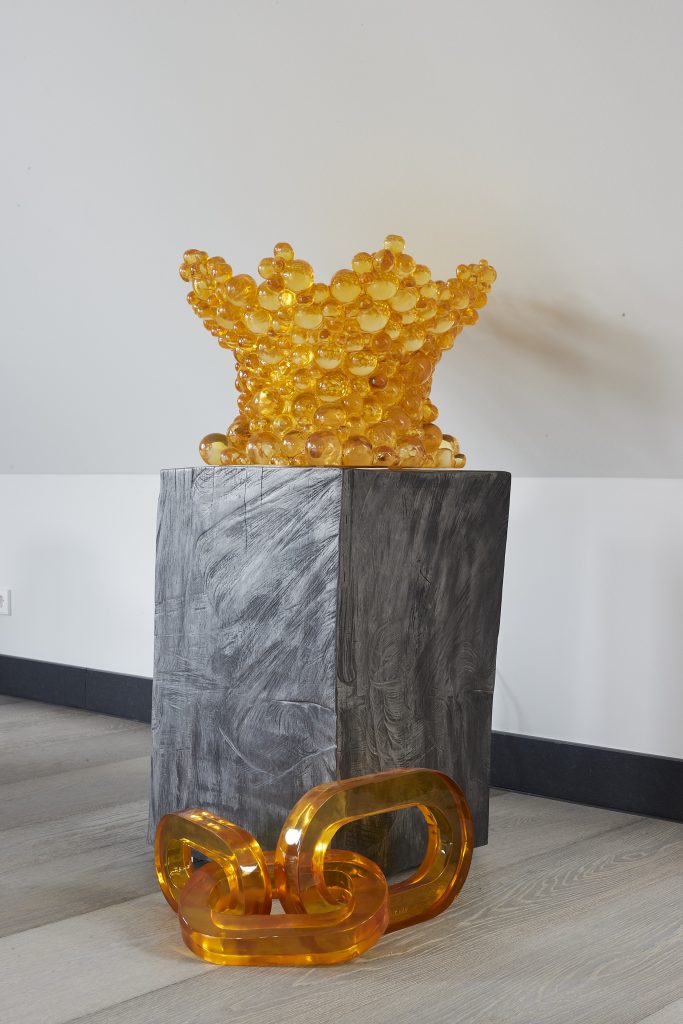 Two citrine colored sculptures by Cedric and Pierre Koukjian, one on a pedestal and another that is three large-scale chain links on the floor next to it.