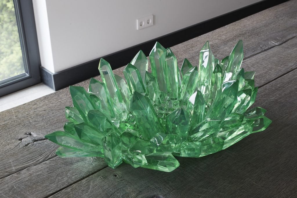 A closeup of a glass-green sculpture installed on a wooden floor by Cedric and Pierre Koukjian that looks like growing crystals.