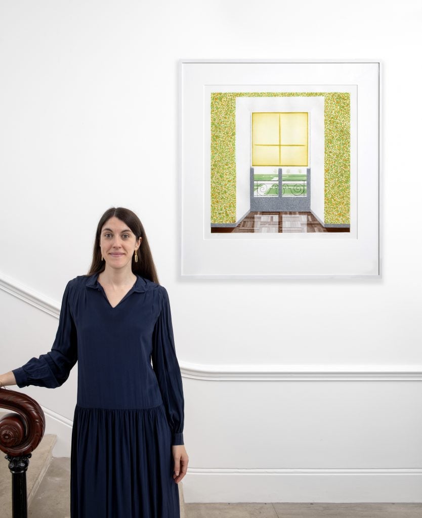 Laetitia Guillotin photographed at Artnet Auctions location at Cromwell Place, London, with a print by David Hockney installed on the wall over her shoulder.