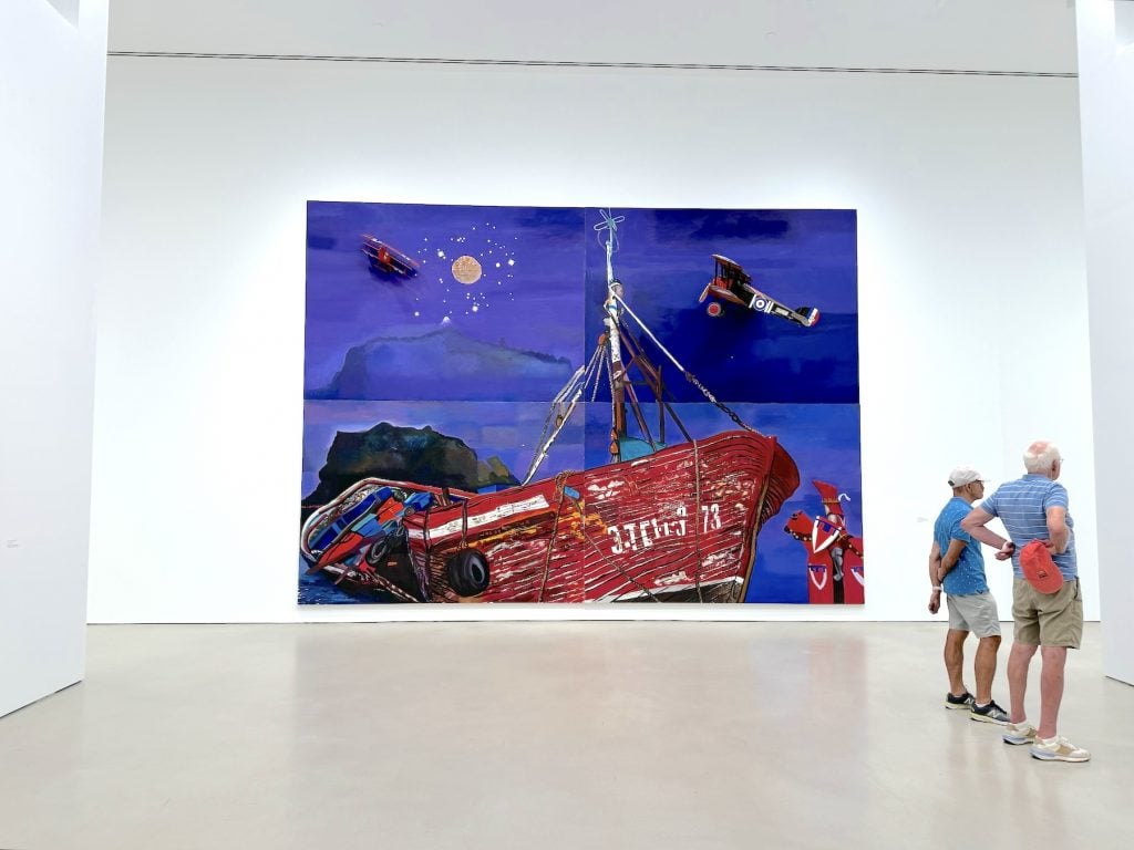A large painting of a boat beneath a blue sky in an art gallery