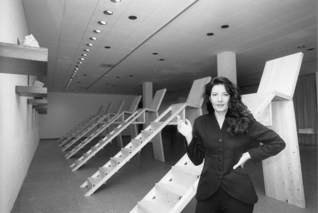Artist Marina Abramović standing in a gallery filled with wooden sculptures
