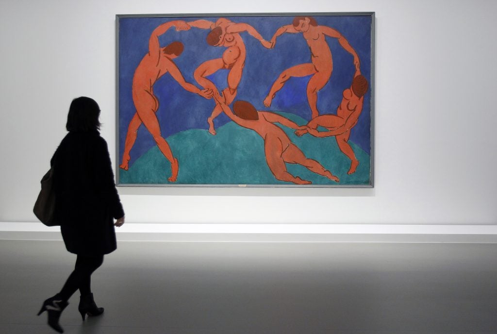 A woman looking at Henri Matisse's The Dance in a gallery. The painting shows five nude figures dancing in a circle