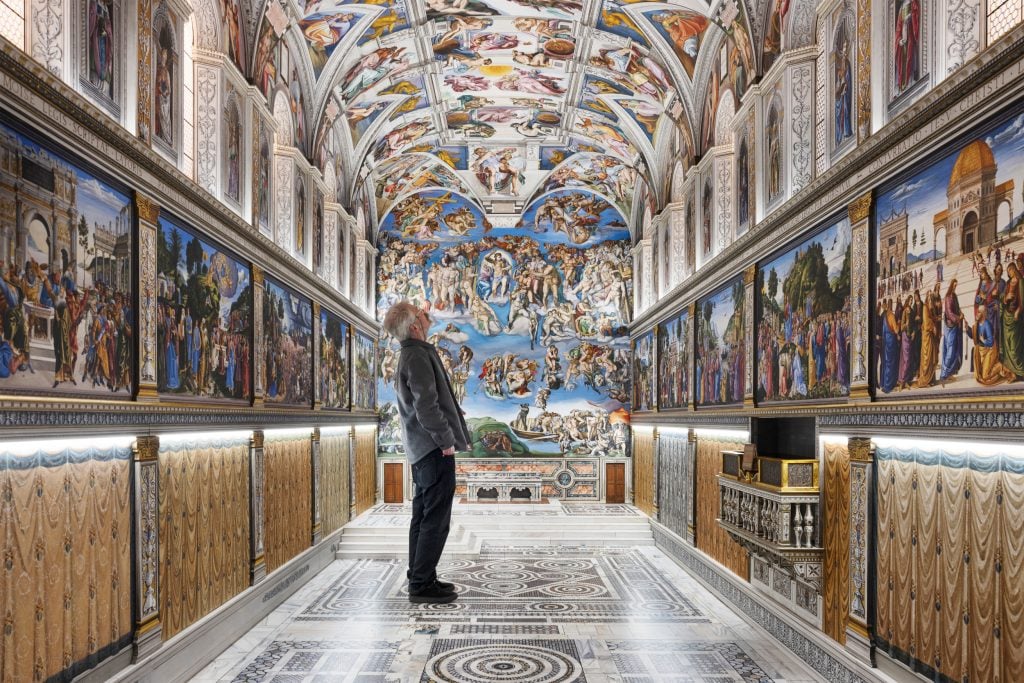 a man is standing inside a room that is frescoed like the sistine chapel but clearly its a copy that is much smaller