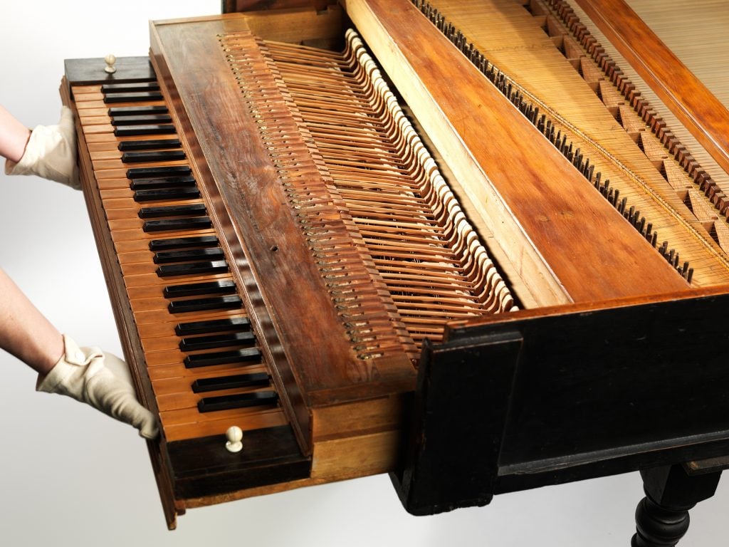 A pair of gloved hands pulling out the keyboard of a brown grand piano