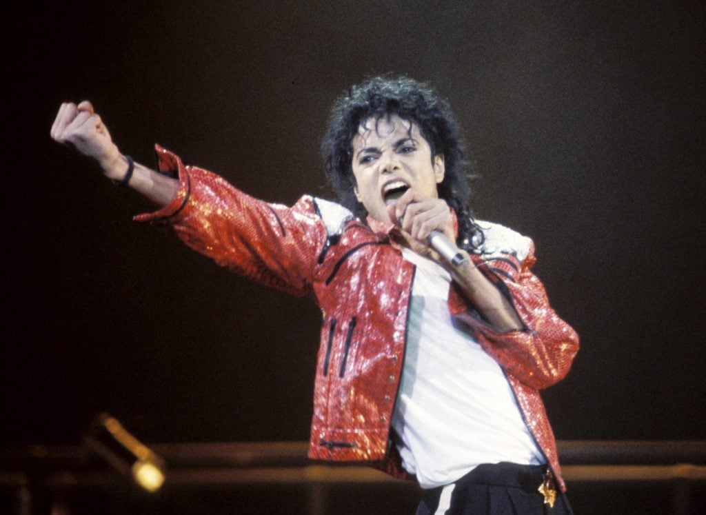 Singer Michael Jackson gesturing and wearing a red leather jacket on stage