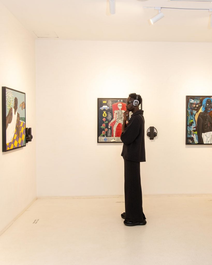 A man wearing headphones looks at artwork on the wall