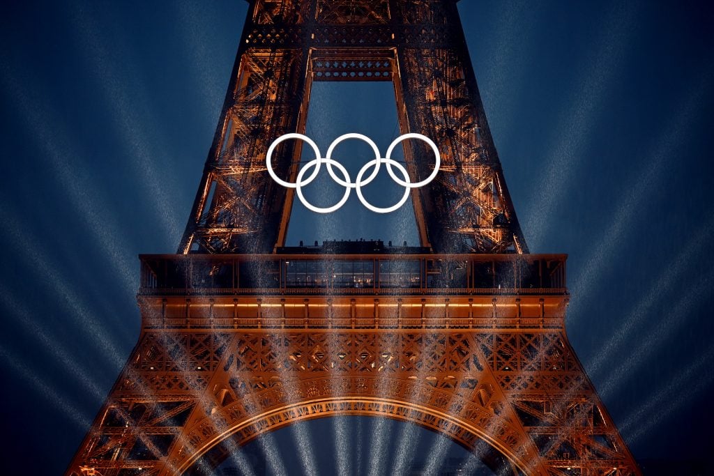 Close up of the Eiffel Tower, hung with the Olympic rings logo, with light pouring in from the background