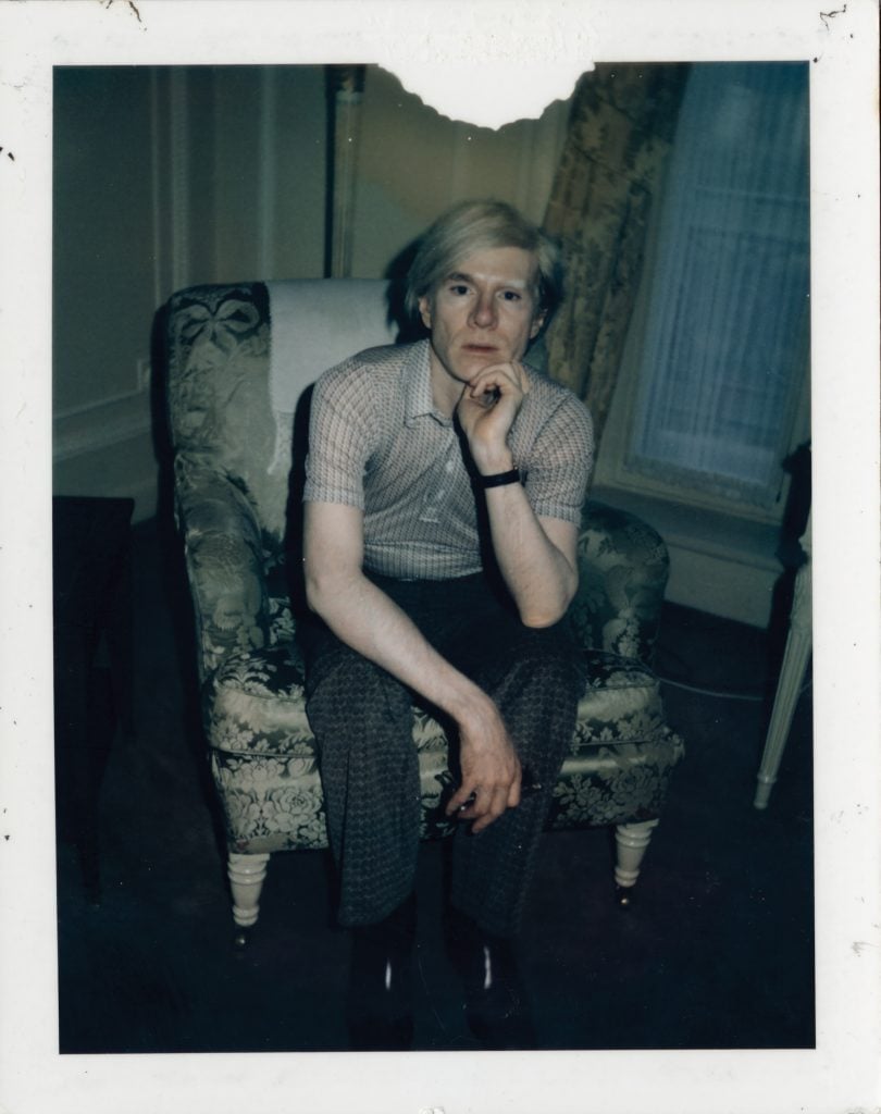 Artist Andy Warhol seated in a chair