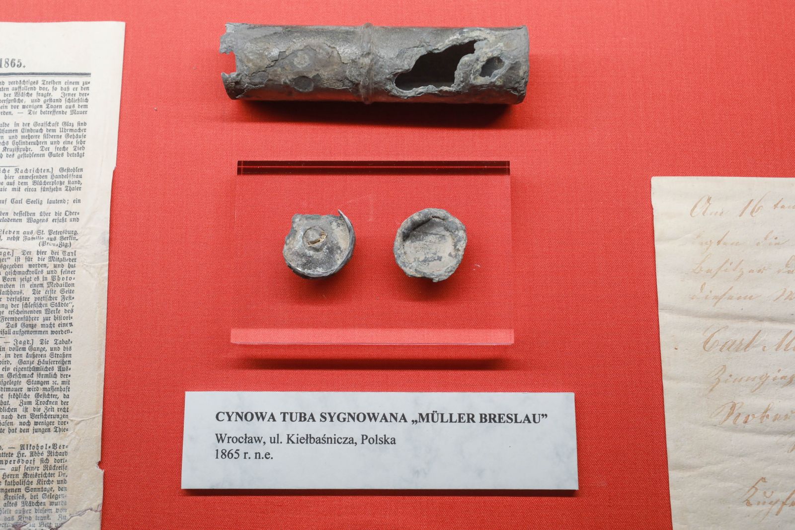 A metal time capsule and two metal caps displayed against a red background