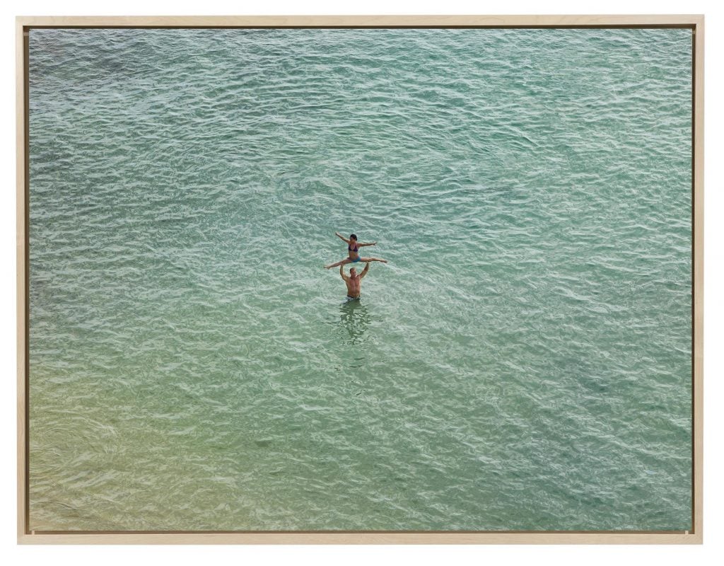 A zoomed out photo of ocean waters with a man standing and holding a woman in a split over his head, featured in the Jane Fonda and Gagosian exhibition.