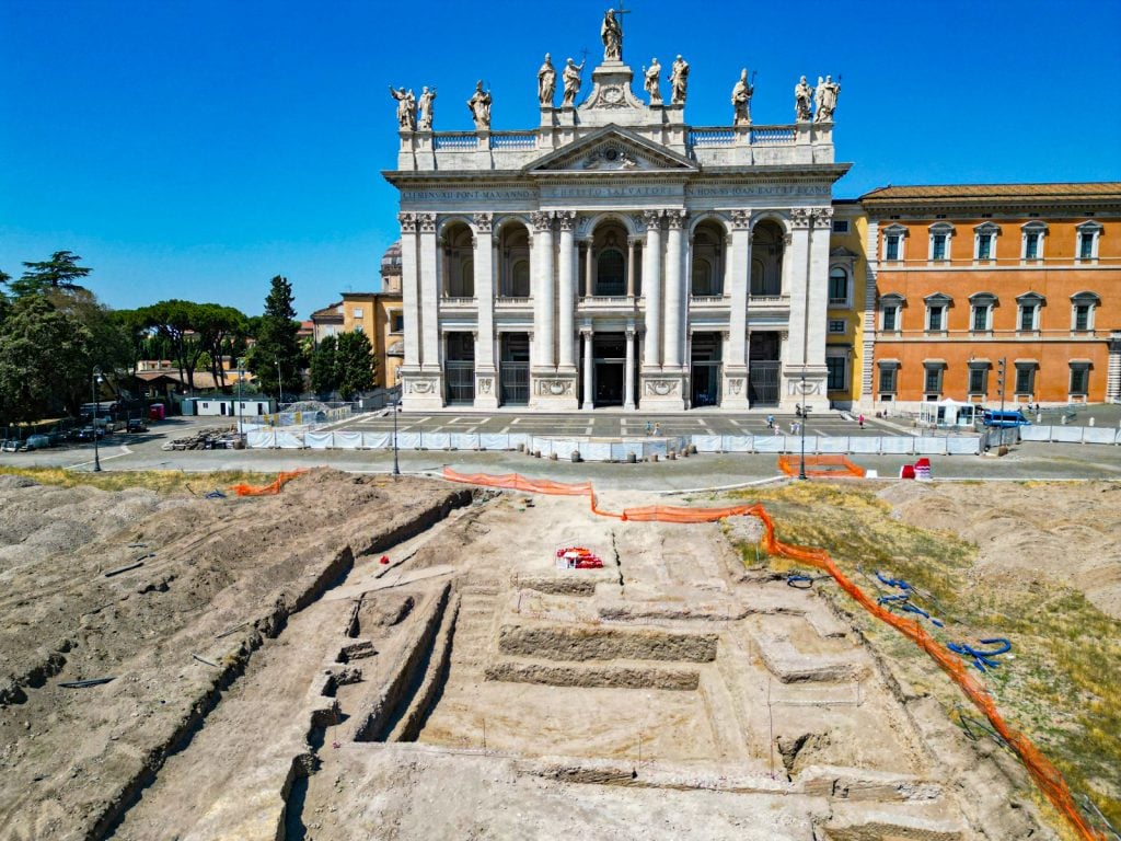 A view of an archaeological dig in Rome, with a basilica in the background