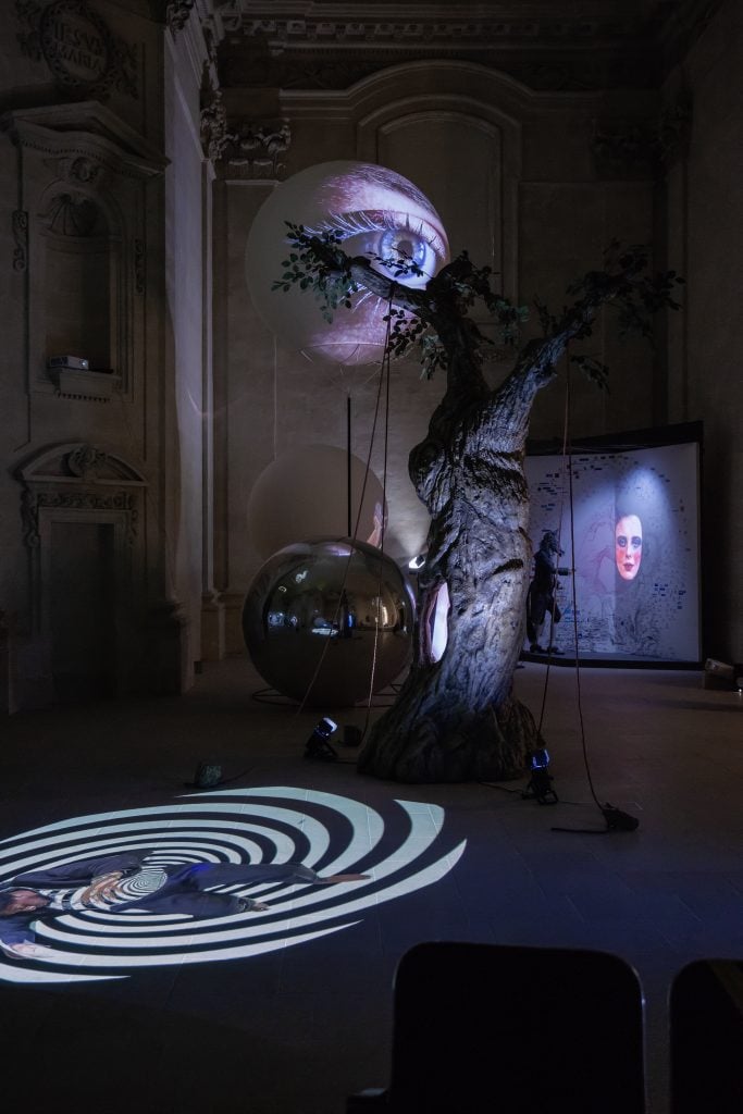 An installation view of art by TOny Ourseler with projections and a globe in a darkened gallery space, recreated in the collab with Pascal Rousseau