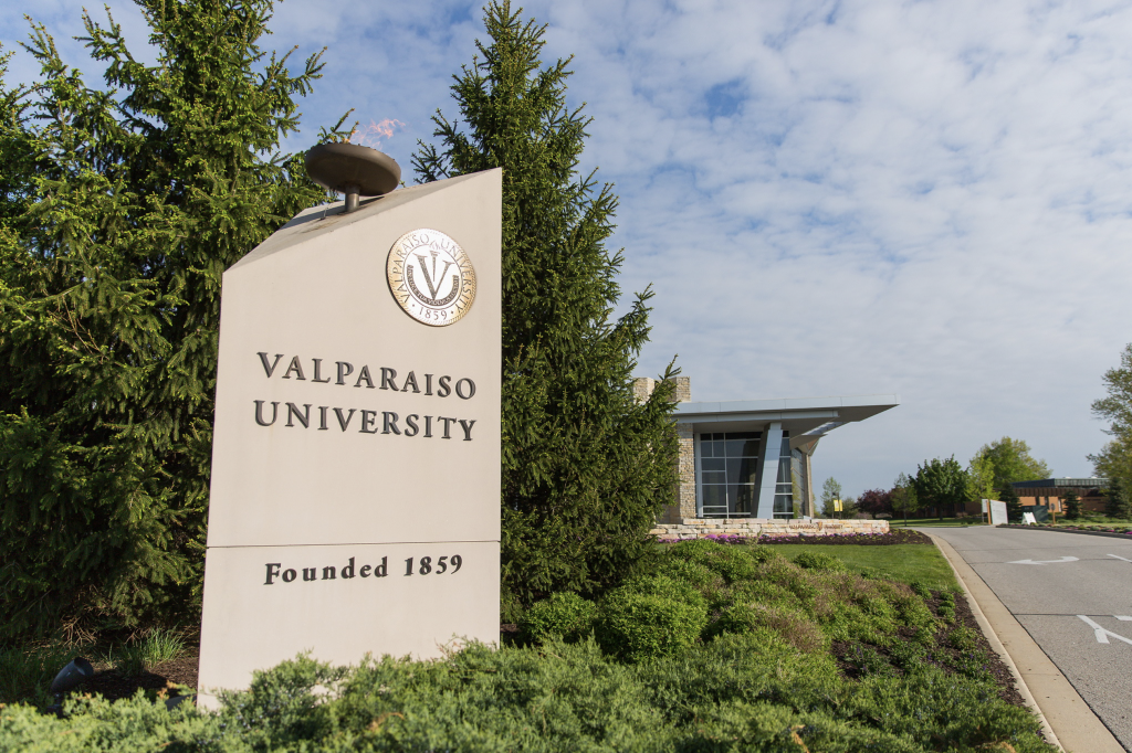 A sign with the words Valparaiso University founded 1859 with trees and a building