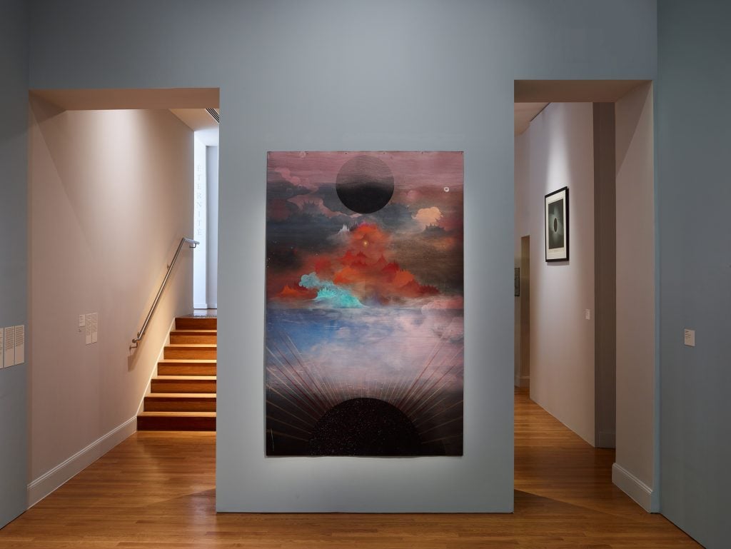 An abstract canvas of clouds and circles hanging in a gallery
