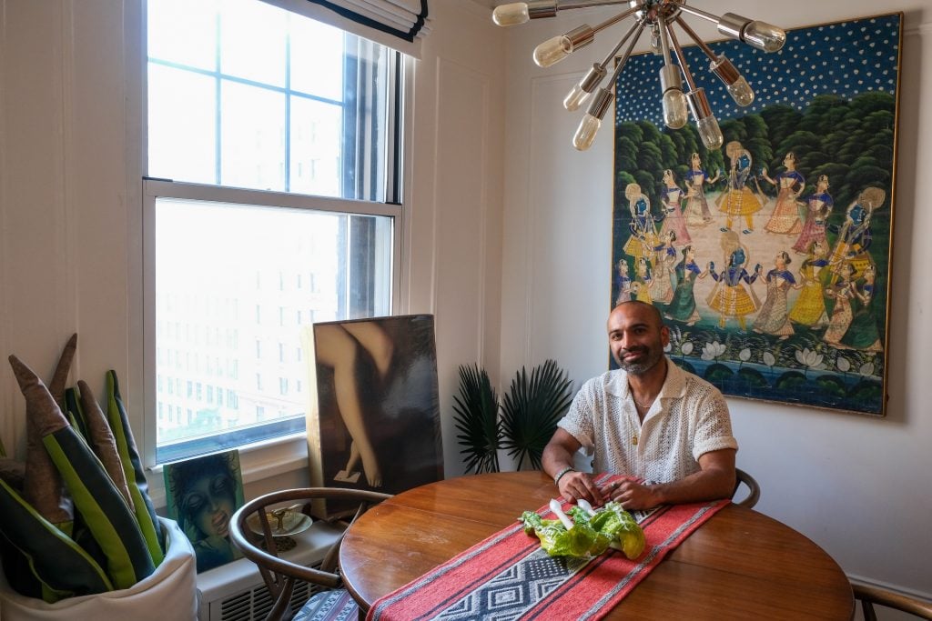 A man sits in a room with several artworks.