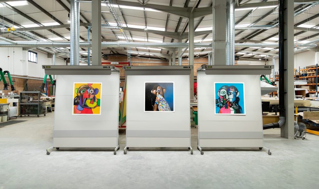 three screen prints are displayed in a large warehouse studio