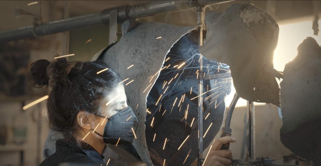 the Italian artist Giulia Cenci is shown welding her art in a Facemask with sparks flying 