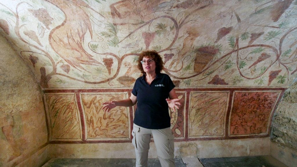 a woman posing in front of an ancient wall painting