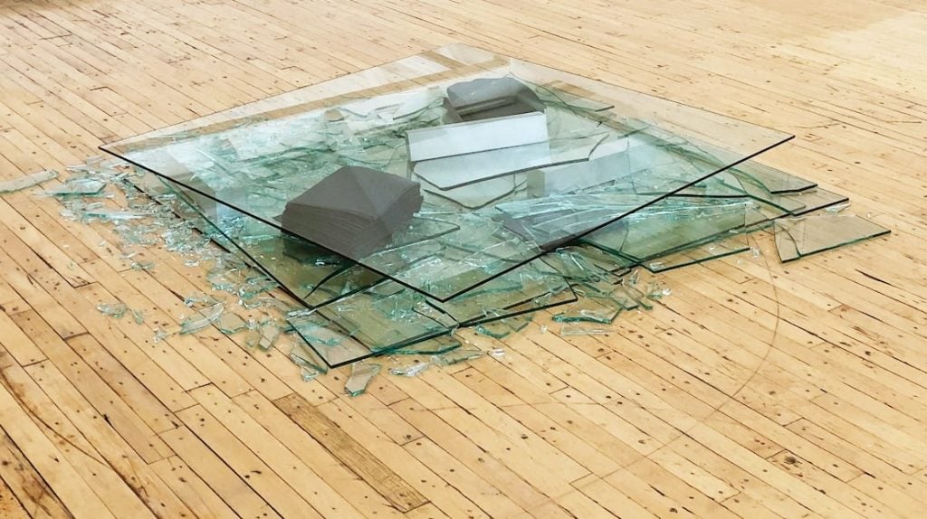 layers of glass panes, some in tact, and some in fragments are seen against a wooden floor.