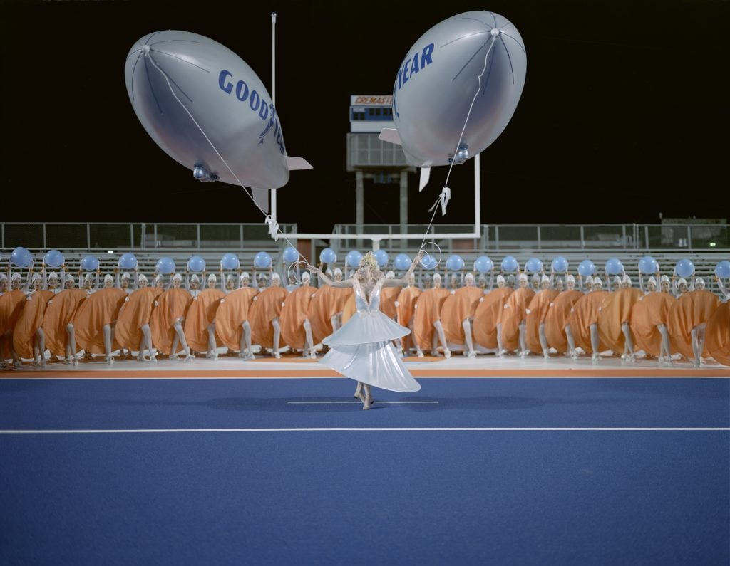 a woman holds two Goodyear blimps in a football field in a art film still from Matthew barney's cremaster 1 