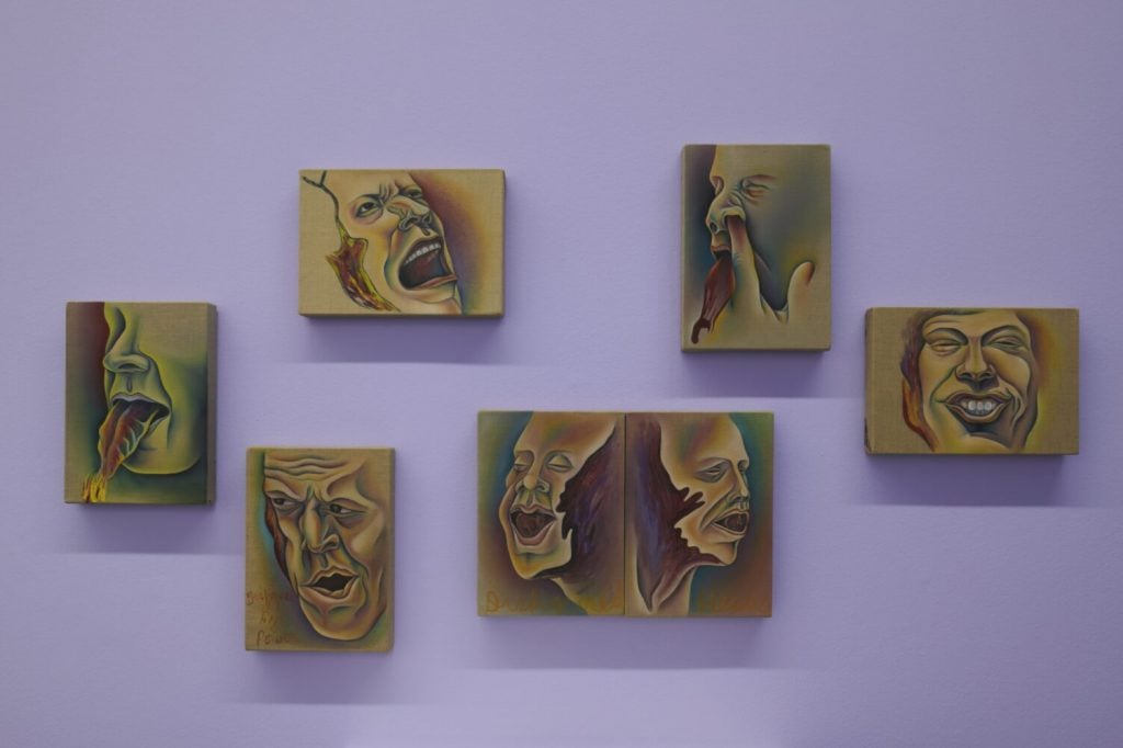 a purple wall has images of contorted faces in apparent distress on the wall