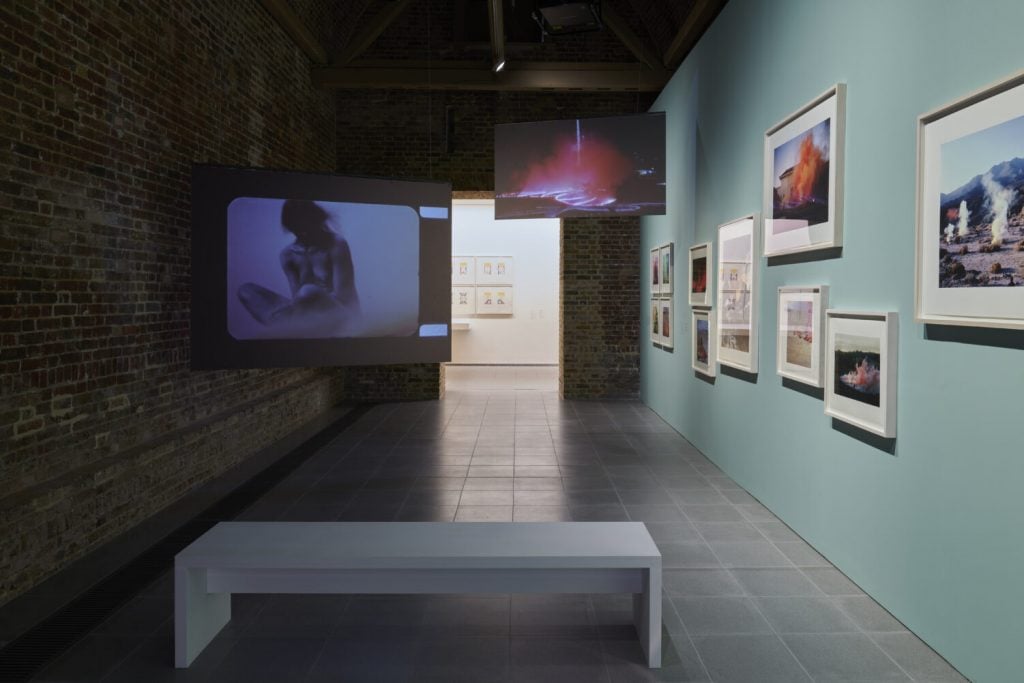 a gallery space has framed images on the wall and some screens showing projected images