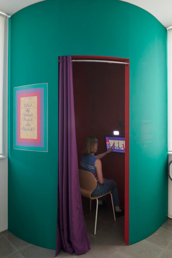 a woman touches a screen inside a little green annex in a larger gallery space