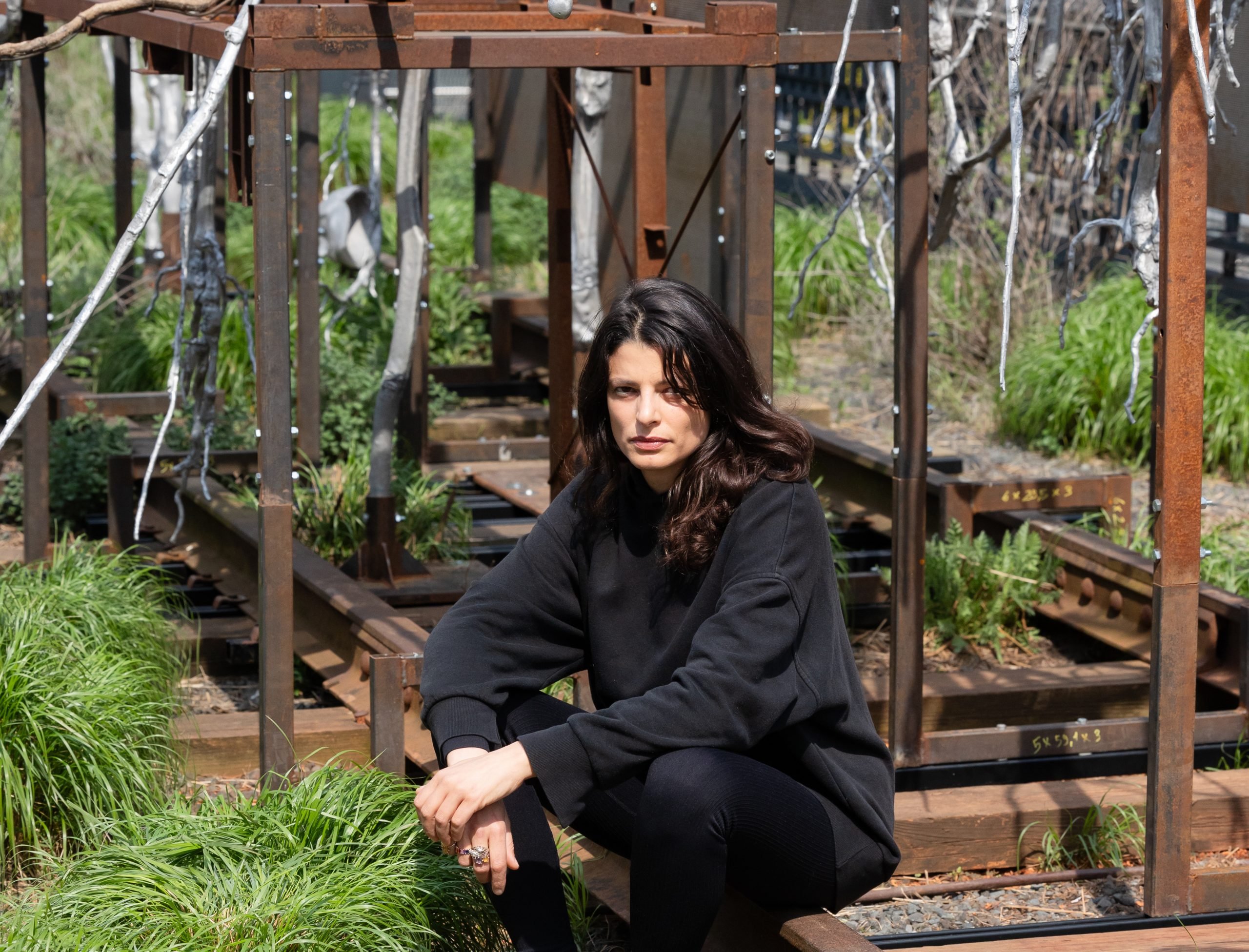 the artist Giulia Cenci squats in front of her work in the exterior of the highland