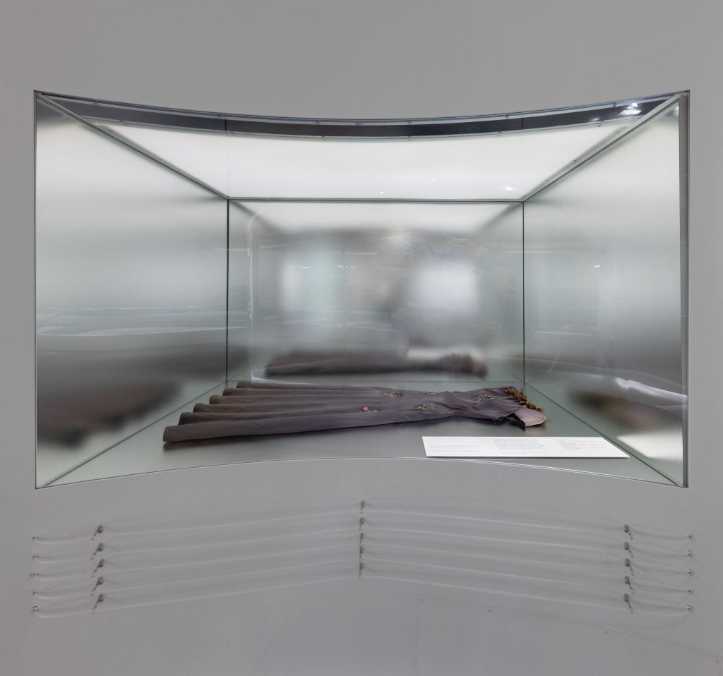 a dress lies in a vitrine, clear tubing is beneath it 