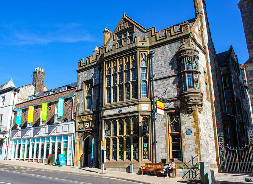 A photograph of an old stone building from the street, with blue skies behind it