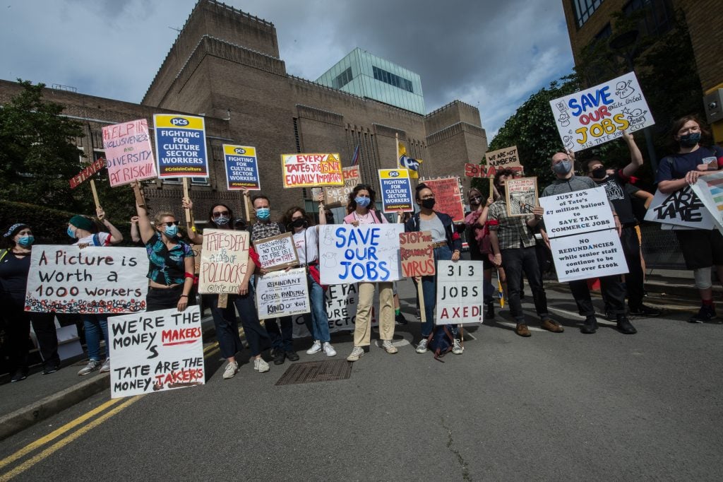a group of people with protest signs stand outside of a large building in London.