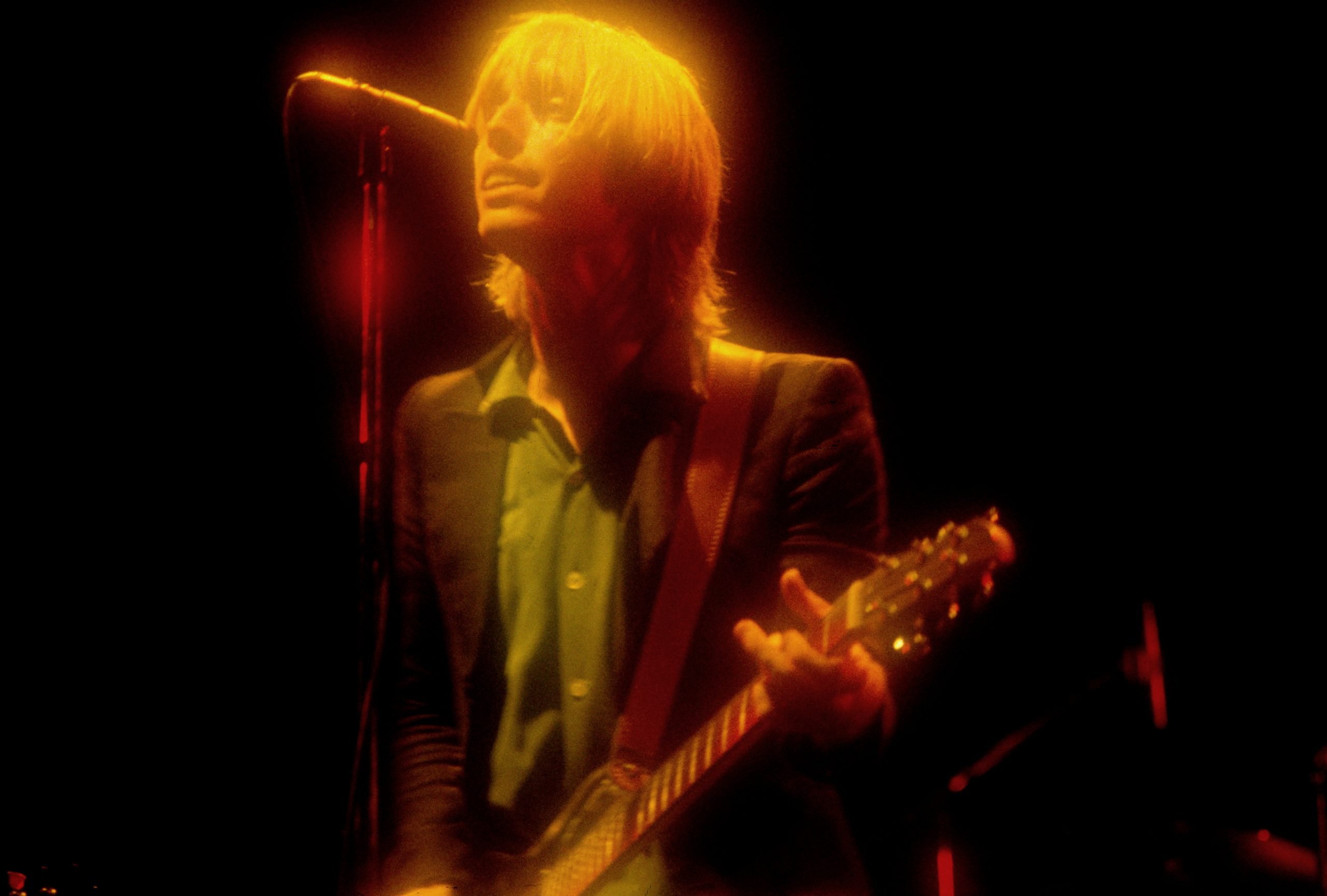 A rock star performs on stage with a guitar, and is lit up with glowing stage lights