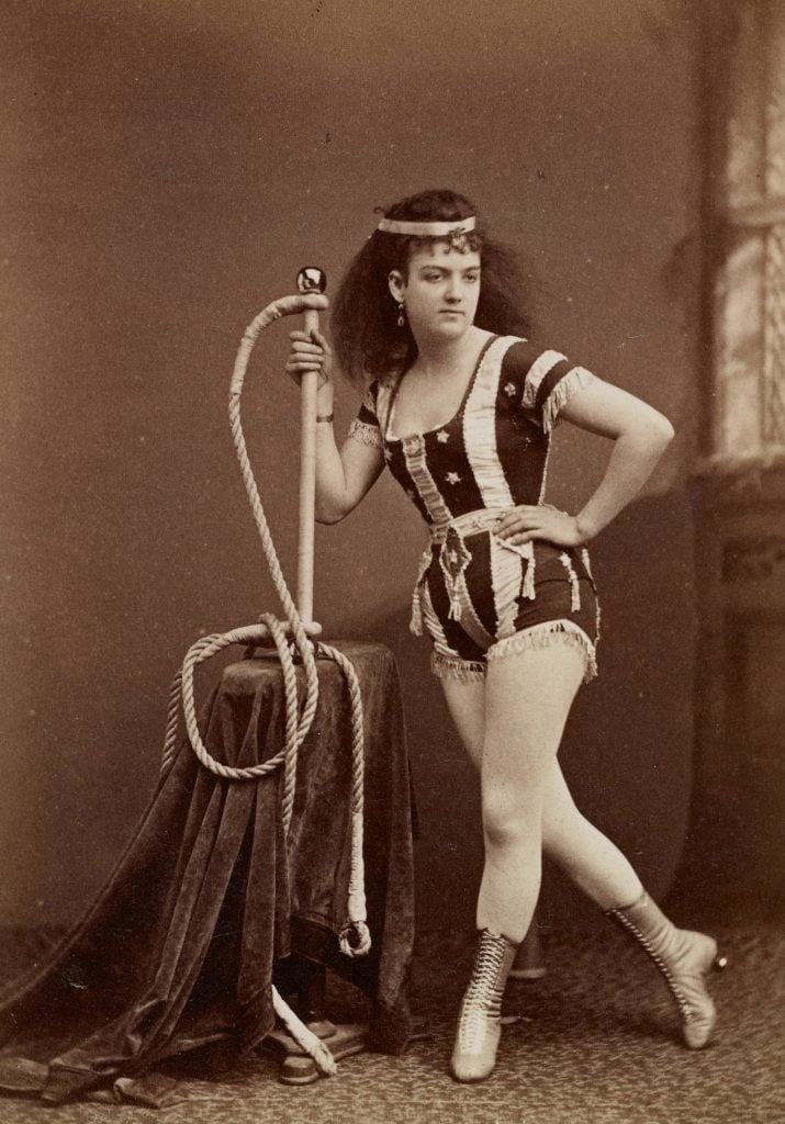 a black and white photograph of a woman in a trapeze outfit with laced boots