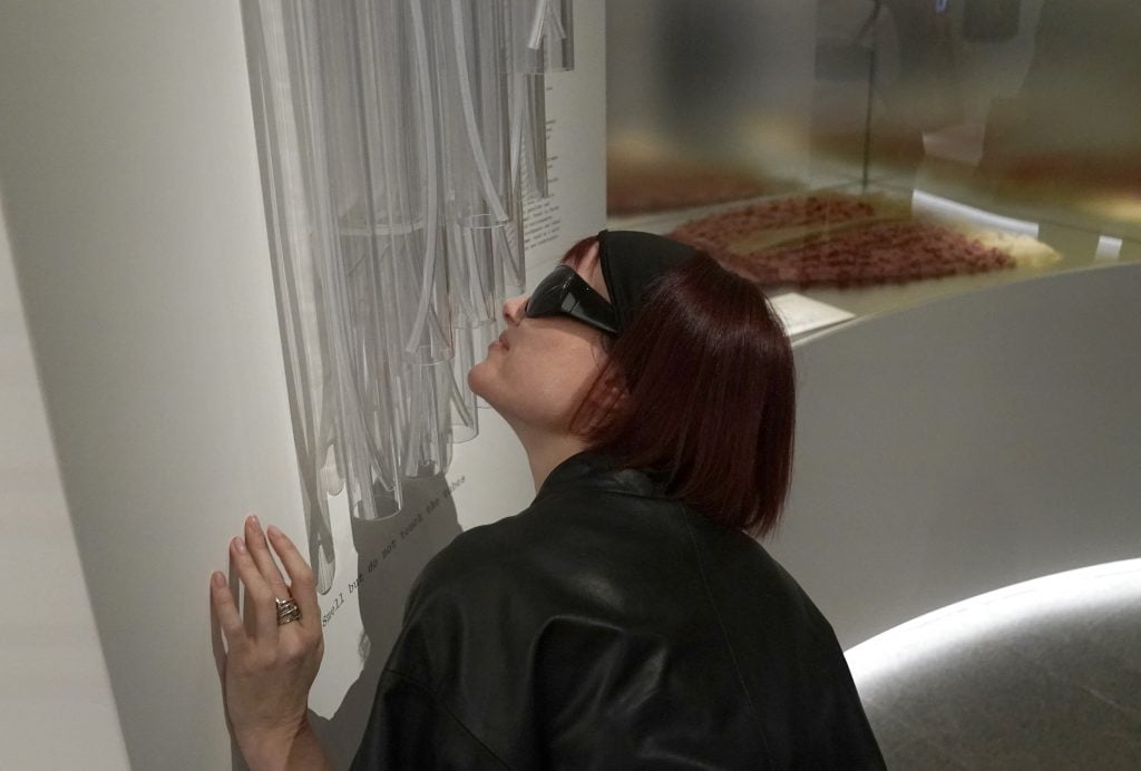 a woman in sunglasses smells clear tubes in a museum 