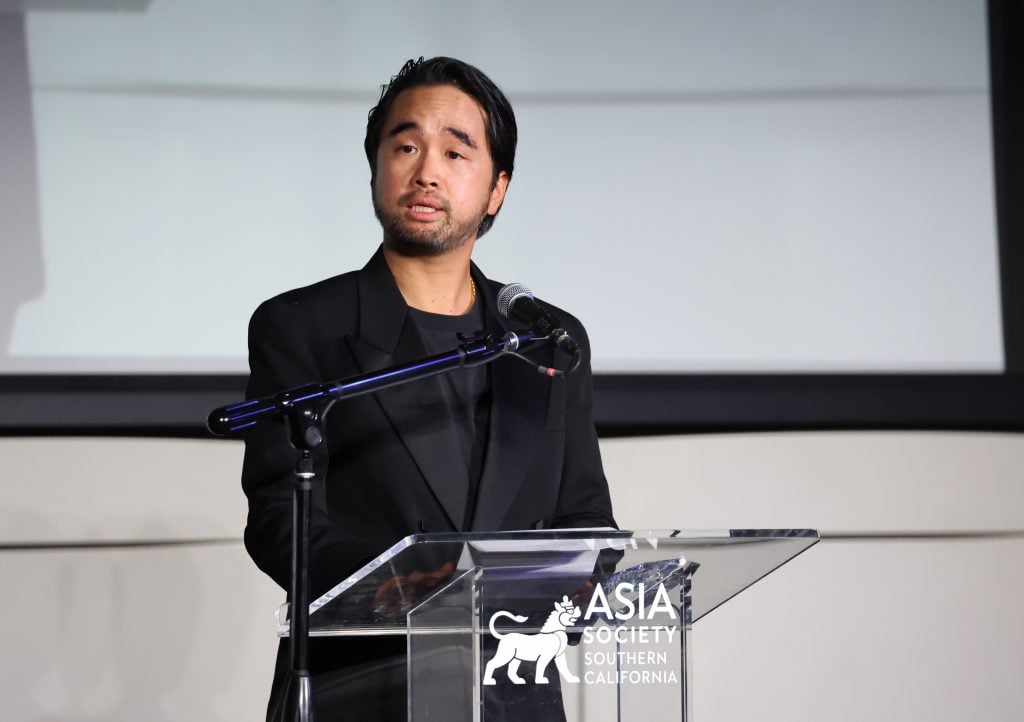 a man in a black suit stands at a clear podium