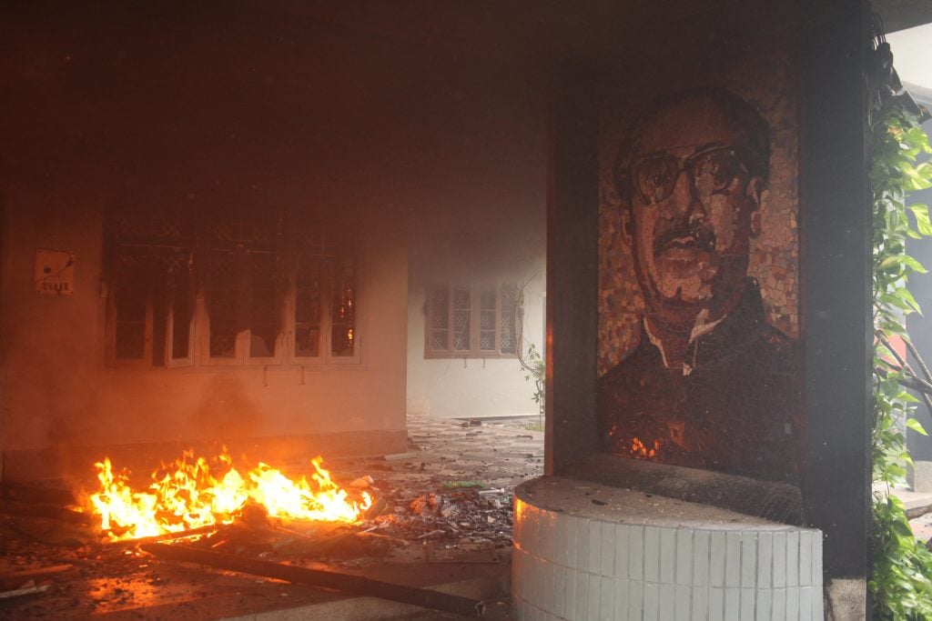 a portrait of a man can be seen near a raging fire and thick smoke billows out from a building behind