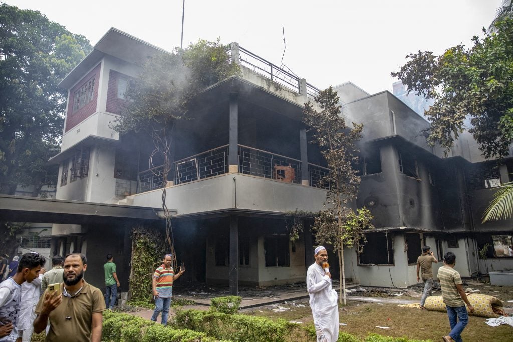 a building that has recently been on fire and appears visibly scorched and damaged, with some people milling around, it is daytime