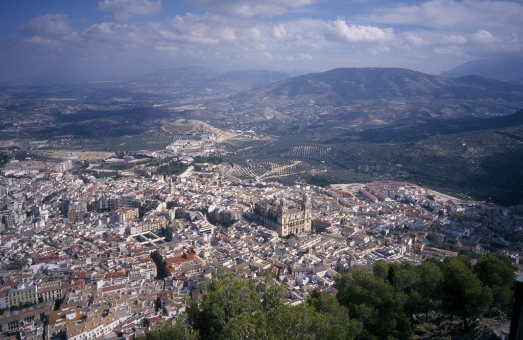 an aerial view of the Jaen region of spane. hills can be seen in the distance against a blue sky. there is a town with a large catherdral in the centre