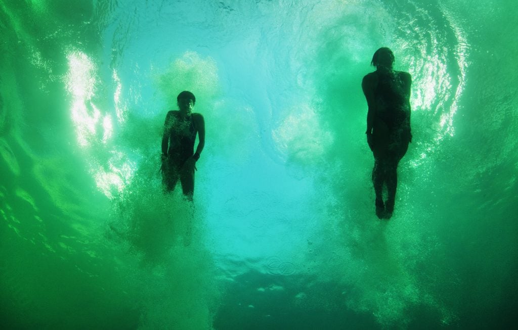 An underwater shot of Kuk Hyang Kim and Mi Rae Kim of Democratic People's Republic of Korea after completing a synchronized dive at the Olympics. The pool had turned bright green. The divers are seen as darkened silhouettes in the murky water.