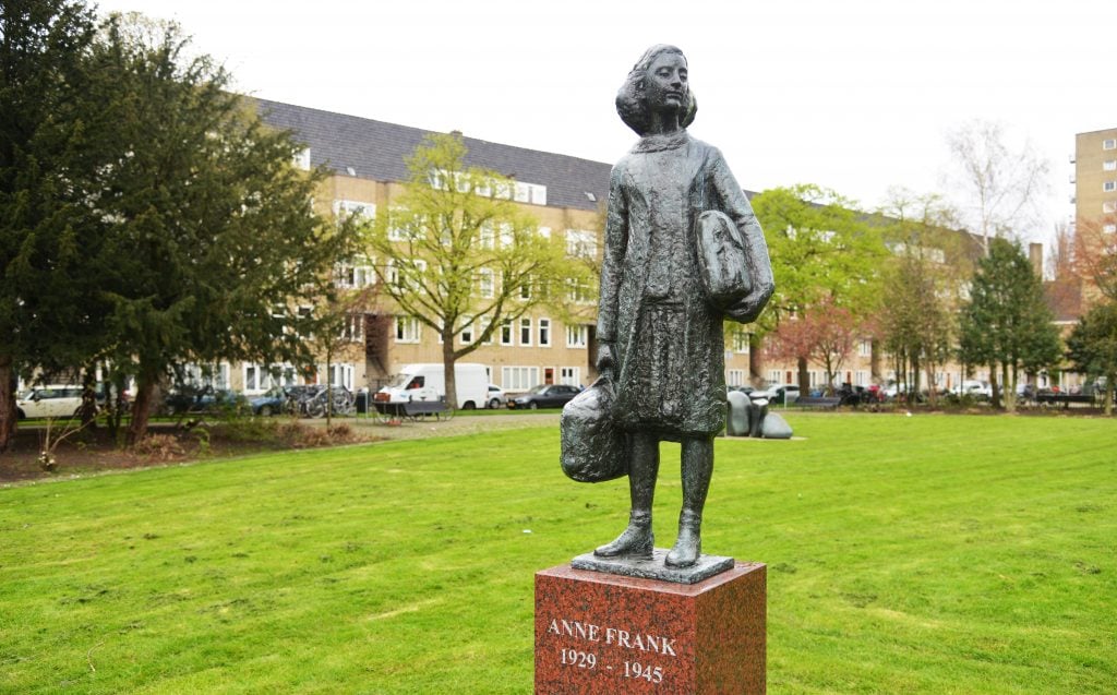 a statue of a young girl stands in a green space with residential housing behind