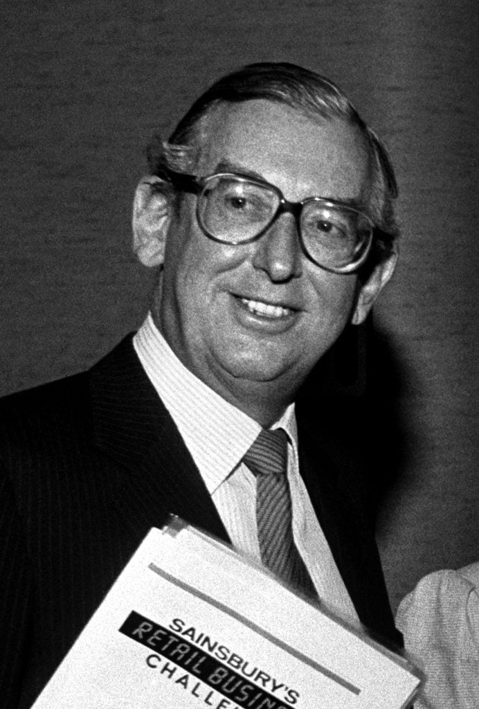 a black and white photo of John Sainsbury holding folder