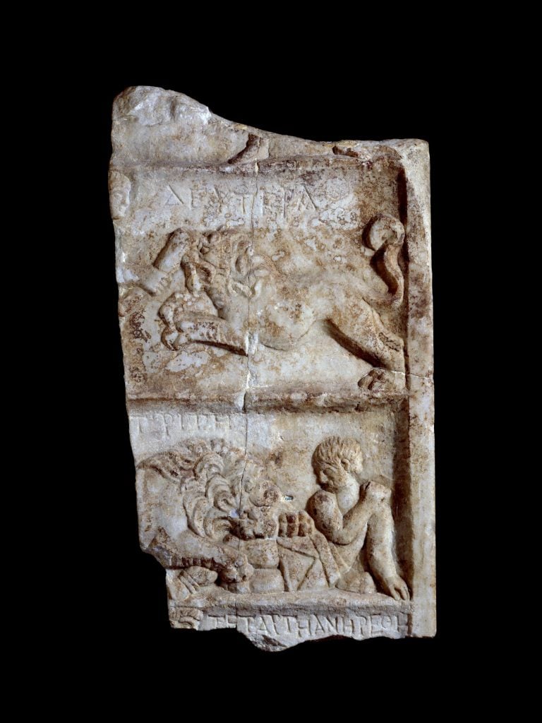 a slab of marble on a black background, scenes with figures can be vaguely seen carved in relief onto the marble