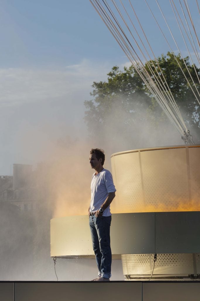 Mathieu Lehanneur with his Paris 2024 Olympic Cauldron by day, surrounded by mist coming off of the sculpture.