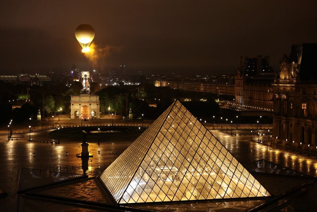 Mathieu Lehanneur's 2024 Olympic Cauldron, an illuminated air balloon floating in the skies of Paris above the Louvre Pyramid and the Arc de Triomphe du Carrousel. 