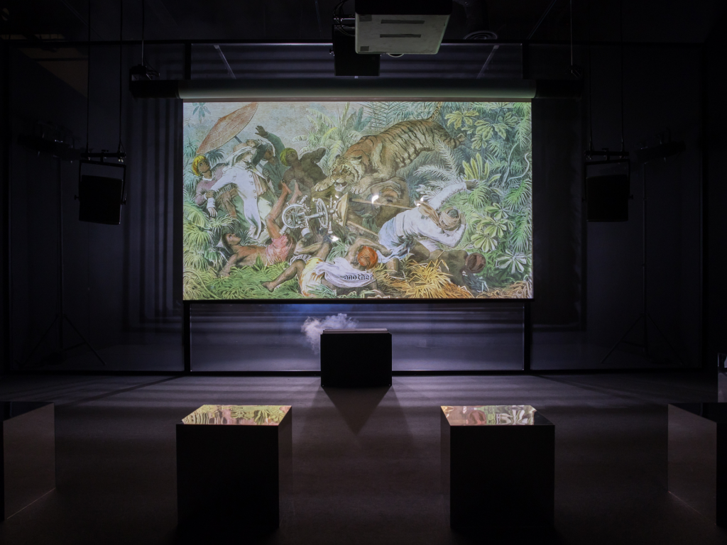 a screen showing an illustration of a tiger amid foliage is seen in a darkened room