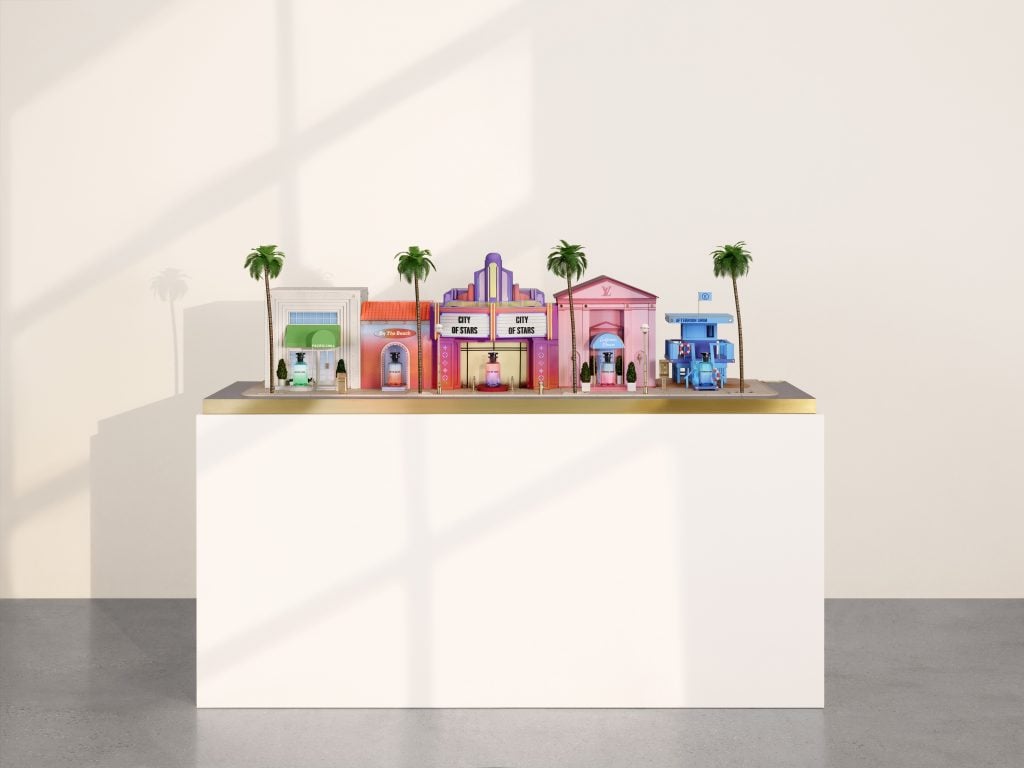 A photograph of a pastel diorama by Alex Israel for Louis Vuitton that depicts an imagined, glamorous Los Angeles street sitting atop a white pedestal before a white wall